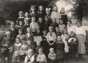 Groepsportret no. 1 van leerlingen en onderwijzend personeel van de openbare lagere school te Lutten aan de Dedemsvaart. Links zit hoofdonderwijzer Hendrik Lanting met achter hem meester Pieter van der Mei. Rechts juf Johanna Reinink met knoopjesblouse en daarnaast juf Elisabeth (Betsy) Rodink.